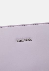 Ljust lavendelfärgad syntetisk material med en texturerad yta, med en silverfärgad "Calvin Klein"-logotyp prägad i mitten.