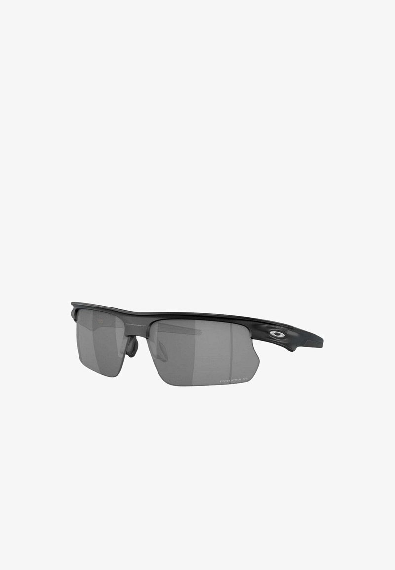 Gafas de sol deportivas con un marco negro mate, lentes grises, forma ergonómica y almohadillas nasales ajustables. Presentan un acento ovalado del logo en los laterales.