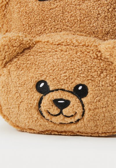 Peluche en forme d'ours en peluche marron avec une fourrure texturée, des caractéristiques faciales brodées et des oreilles arrondies. Matériau doux et duveteux.