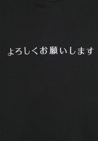 Bílý japonský text "よろしくお願いします" vyšitý na černé tkanině, centrovaný a horizontálně zarovnaný.