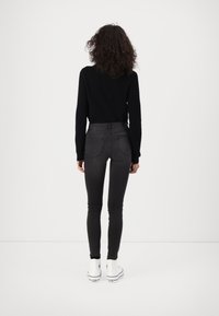 Jeans skinny negros de tiro alto con un diseño elegante y dos bolsillos traseros, combinados con un suéter texturizado negro y zapatillas blancas.