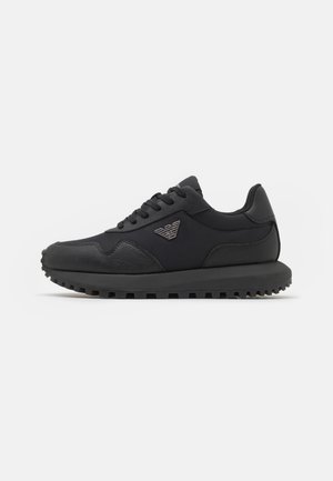 Czarny niski sneaker z teksturowaną podeszwą, sznurowanym przodem i srebrnym logo orła z boku, na jednolitym białym tle.