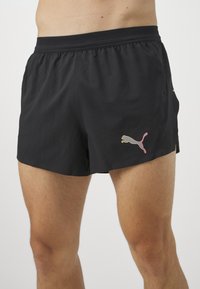 Czarne spodenki sportowe z elastycznym pasem, posiadające siatkową sekcję oraz wielokolorowe logo Puma na dolnym lewym boku.