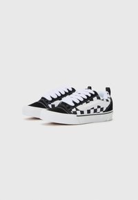 Svartvita rutiga kanvas sneakers med vita snörningar, gummisula och en kontrasterande svart tåskydd. Hållbar design med låg profil.