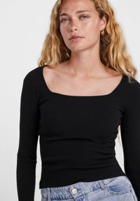 Top manica lunga nero a coste con scollatura quadrata. Si adatta bene, con una consistenza morbida e un design semplice. Indossato con jeans azzurri chiari.