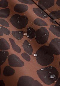 Vandafvisende brunt stof med store sorte leopardpletter, prydet med vanddråber på overfladen, der fremhæver den glatte tekstur.