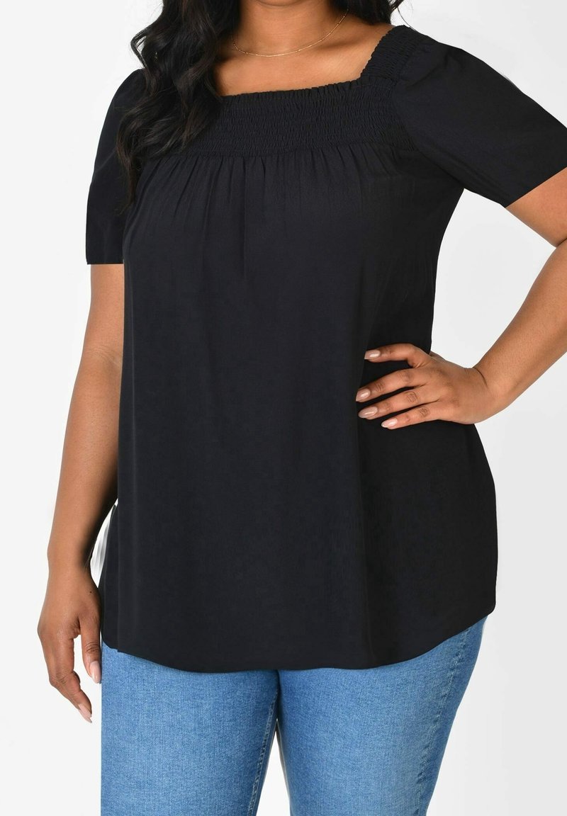 Top nero con maniche corte e scollatura quadrata, caratterizzato da arricciature sul petto. Abbinato a jeans in denim blu chiaro.