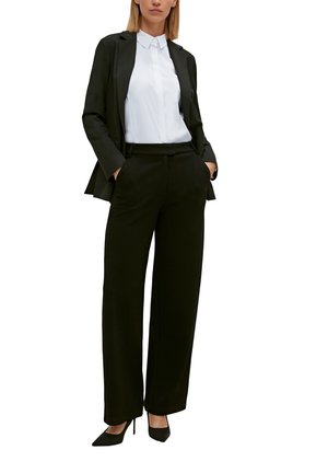 Schwarzer maßgeschneiderter Blazer über einem weißen Hemd mit Knöpfen, kombiniert mit schwarzen Palazzo-Hosen und schwarzen High Heels.