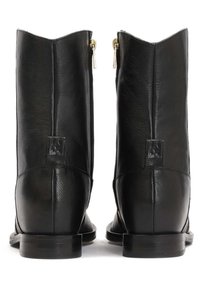 Bottes chevilles en cuir noir avec une finition brillante, bout arrondi et détail de fermeture éclair dorée à l'arrière. Talon plat avec semelle textur ée.