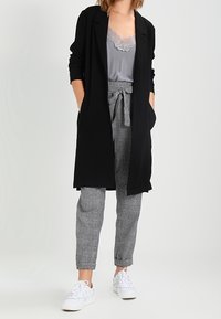 Svart lång blazer, grå topp med spetskant, grå byxor med houndstooth-mönster, vita sneakers, avslappnad passform, mjuka texturer.