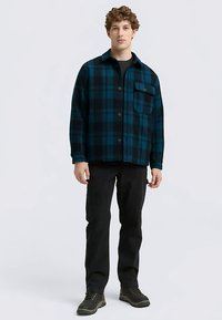 Mėlynas ir juodas languotas flanelinis marškinys su ilgomis rankovėmis, užsegamas sagutėmis priekyje, vieninteliu krūtinės kišene, dėvimas ant juodų marškinėlių ir juodų kelnių.