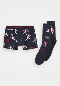 Mornarske gaće i odgovarajuće čarape sadrže blagdajne uzorke Djeda Mraza i natpis "MERRY XMAS". Elastična traka u struku s brendiranjem "JACK & JONES".