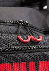Black textured backpack with red zipper pulls and accents. Features a prominent logo in red, highlighting its design and material details.