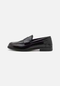 Sorte lærloafers med en rund tå, sydde detaljer og en bred rem over toppen. Flat gummisåle gir stabilitet.