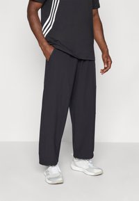 Pantalons noirs amples avec taille élastique, poches latérales et tissu respirant. Associés à un tee-shirt noir avec des rayures blanches.