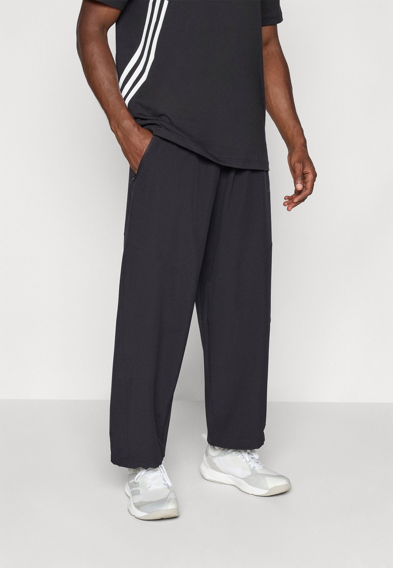 Pantalons noirs amples avec taille élastique, poches latérales et tissu respirant. Associés à un tee-shirt noir avec des rayures blanches.