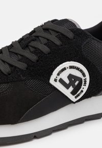 Scarpe da ginnastica nere con un mix di materiali in rete e suede. Include una toppa con logo testurizzato e lacci piatti. Suola intermedia bianca, suola esterna nera.