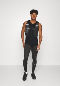 Czarny sportowy top na ramiączkach, czarna kamizelka do biegania z kieszeniami, czarne legginsy. Na kamizelce i legginsach znajdują się logo Puma. Czarne buty sportowe.