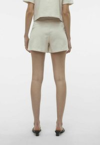 Pantaloni corti in lino beige chiaro con un design su misura, dotati di tasche frontali e un orlo che termina a metà coscia, abbinati a sandali con tacco basso.