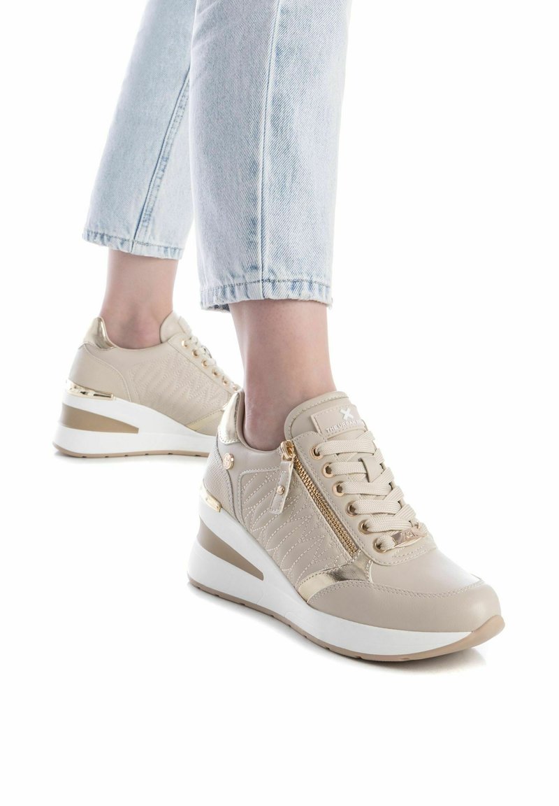 Sneakers con zeppa beige, con una parte superiore testurizzata, dettagli dorati e una zip decorativa. Design leggero con una suola bianca e dorata.