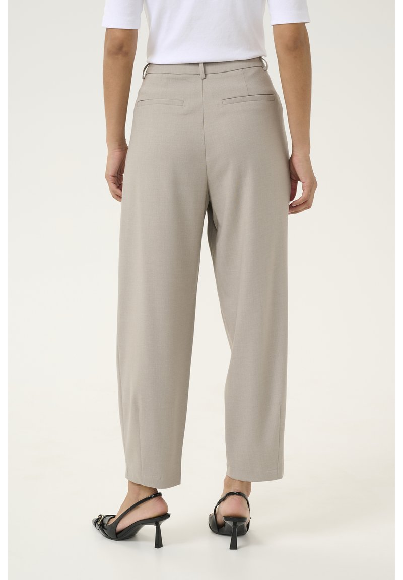 Hellbeige weite Hosen mit glatter Textur, ausgestattet mit Gürtelschlaufen und zwei Gesäßtaschen. Kombiniert mit schwarzen, offenen Sandalen mit Absatz.