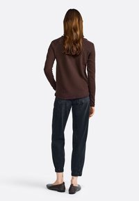 Braunes Langarmhemd kombiniert mit dunkler Jeans, die elastische Bündchen hat, und dunklen braunen Ballerinas, von hinten gesehen.