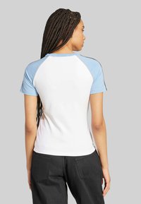 T-shirt kratkih rukava s raglan krojem, svijetloplavih rukava i bijelog tijela, s crnim obrubom duž ramena. Klasičan kroj, mješavina pamuka.