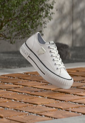 Pantof sport din piele albă cu accente negre, vârf rotund, talpă plată și nervuri în relief. Prezintă un detaliu cu logo pe lateral și închidere cu șireturi.