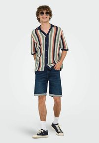 Camisa de manga corta con un patrón a rayas en verde, naranja y azul marino, combinada con pantalones cortos de denim enrollados y zapatillas azul marino.