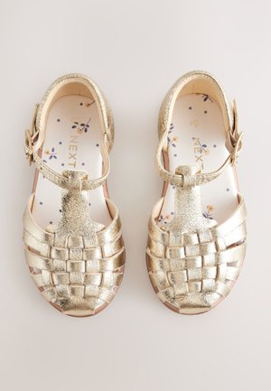 Goudkleurige metallic sandalen met een geweven bovenzijde, gesp sluiting en een patroon in de binnenzool met kleine bloemmotieven op een lichte achtergrond.
