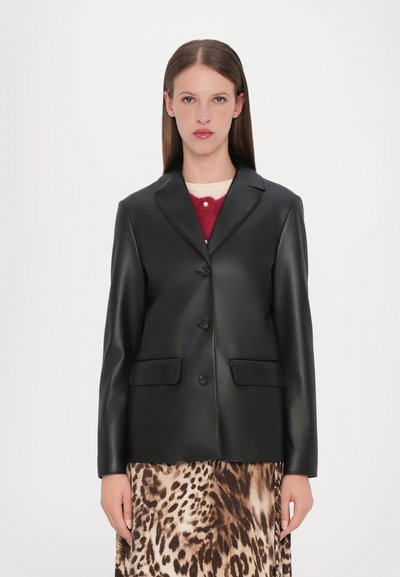 Zwarte faux leren blazer met een gesneden kraag, twee voorzakken en drie knopen. Gedragen over een rok met luipaardprint. Glad textuur.