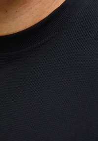 Κοντινό πλάνο του λαιμού ενός σκούρου, υφασμάτινου πουλόβερ με πλέξη και ενός μέρους γυμνού δέρματος πάνω από τον γιακά.