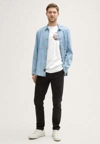 Lys blå denimskjorte over en hvid grafik T-shirt, parret med sorte bukser og hvide sneakers. Casual outfit med varierede teksturer.