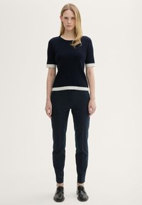 Námořnický úpletový top s krátkým rukávem s bílými detaily na manžetách a lemu, spárovaný s tmavými slim-fit kalhotami a černými šněrovacími botami.