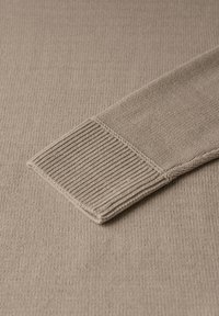 Beige strikket sweaterstof med ribbet manchet. Teksturen er glat, og har et subtilt mønster samt en ensartet farve gennem hele stoffet.
