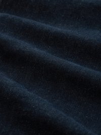 Dunkelblauer Denimstoff mit sichtbarer Struktur und weichen Falten, die sanfte Schatten auf der Oberfläche erzeugen.