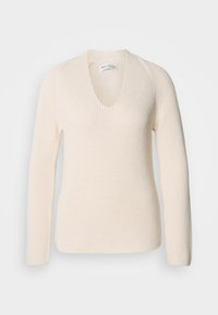 Κρεμίνινο πλεκτό πουλόβερ με V λαιμόκοψη, μακριά μανίκια και ριγωτή υφή, που διαθέτει άνετη εφαρμογή χωρίς ορατά σχέδια ή αξεσουάρ.