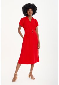 Rotes Kleid mit kurzem Ärmel und Kragen, tailliert mit einem Gürtel mit silberner Schnalle, kniefrei, glatte Textur, kombiniert mit nudefarbenen Blockabsatzsandalen.