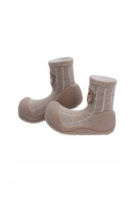 Zapatitos de bebé en suave color beige con suelas de goma flexibles y un upper tipo calcetín de punto, que presenta un pequeño diseño de cara de animal en el lateral.