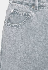 Close-up of light blue denim jeans pocket with metal rivets and visible stitching detail.