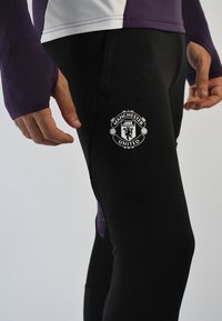 Leggings atléticos negros con el logo del Manchester United en el muslo. Material suave y elástico; diseño ajustado que mejora el movimiento.
