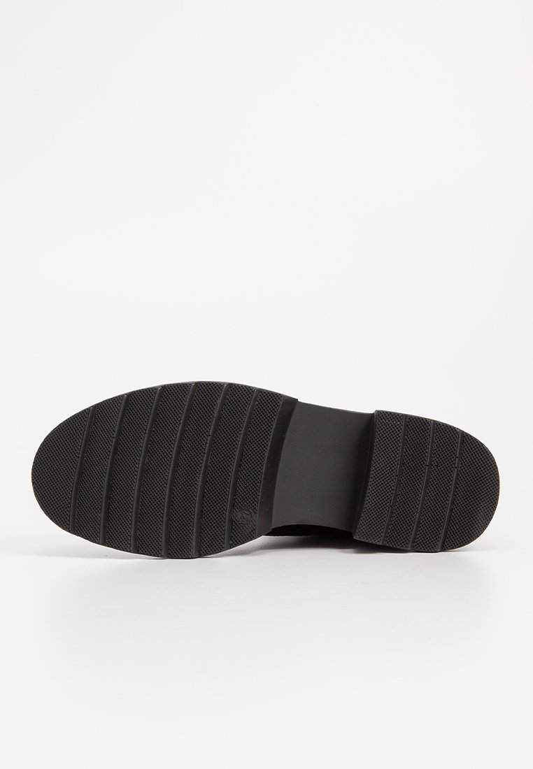 Suola di scarpa in gomma nera con grip testurizzato e righe orizzontali, caratterizzata da una punta arrotondata e bordi lisci, progettata per offrire trazione.