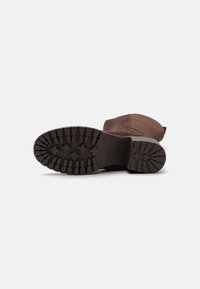 Brune ruskinnsstøvler med en teksturert gummibunn, med et fremtredende spor mønster og en rund tå. Fremhevet av et enkelt design.