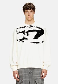 Sudadera blanca con un amplio diseño abstracto negro en la parte frontal. Tiene mangas largas, cuello redondo y un corte relajado.