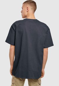 Tmavě šedé oversized tričko vyrobené z bavlny, s kulatým výstřihem, krátkými rukávy a hladkou texturou. Žádné viditelné vzory ani grafika.