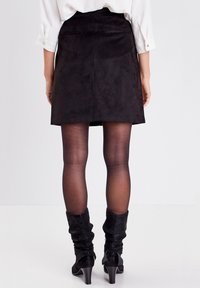 Zwarte suède minirok met een gladde textuur en minimale naden; gecombineerd met doorzichtige panty's en slouchy zwarte laarzen tot de knie.