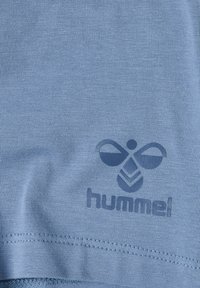 Lichtblauw sportshirt van gladde stof, met een donkerblauw logo en een gestileerd bijontwerp nabij de zoom.