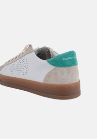 Witte leren sneaker met beige suède accenten, groene hiel tab, geperforeerd ontwerp en bruine rubberen buitenzool. Tekst op de hiel leest "You Can S."