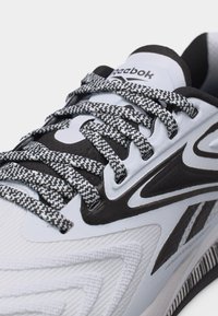 Λευκό και μαύρο αθλητικό παπούτσι Reebok με κορδόνια σε ασπρόμαυρο σχέδιο και υφασμάτινες λεπτομέρειες με υφή στη μύτη και την πλευρά.