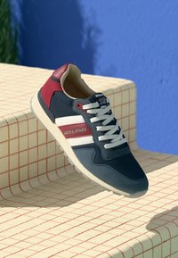 Marineblå og burgunder sneakers med hvide striber, tekstureret stof og polstret sål. Har et logo på siden og snørebåndsdesign.